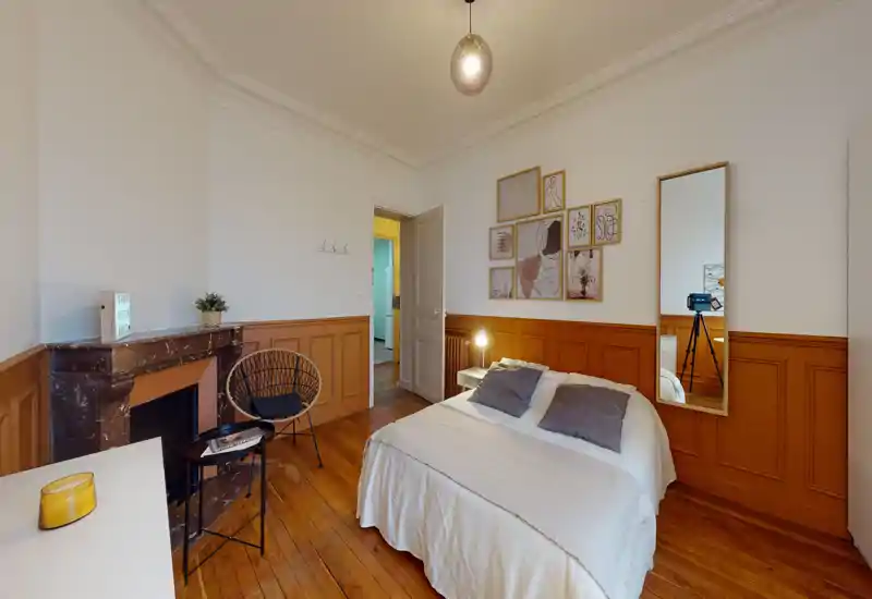 Charming bedroom with a neatly made double bed, warm wooden floors, decorative moldings and tasteful wall art. A full-length mirror and bedside lamp complete this bright, cozy space ideal for restful stays.