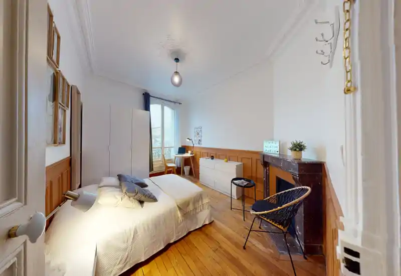 Bright, stylish bedroom with wooden floors, a comfortable double bed, wardrobe and a desk by a tall window. Warm wood panelling and decorative ceiling add character and cozy atmosphere.