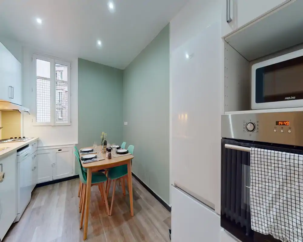 Cuisine en longueur moderne et lumineuse avec électroménagers intégrés et petite table pour quatre — propre et bien mise en scène pour des locations courtes.