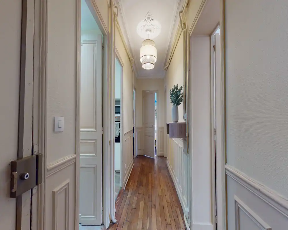 Couloir lumineux et élégant avec parquet, moulures murales et suspensions ; couloir dégagé menant aux pièces intérieures.