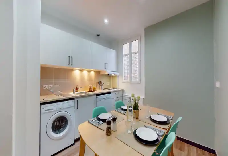 Compact modern kitchen with integrated appliances and a set dining table for four; warm under-cabinet lighting and a large window provide a bright, inviting atmosphere.