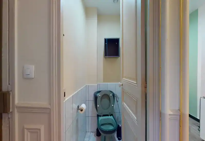 Compact bathroom with a tiled lower wall, a green toilet and wall-mounted shelf; neutral lighting and neat finishes.