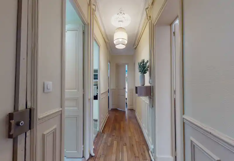 Bright, elegant hallway with wooden floors, decorative wall moulding and pendant lighting; shows a clear corridor leading to interior rooms.