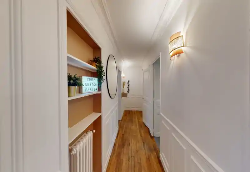Bright, narrow corridor with wooden floors, decorative wall panelling and built-in shelving — a welcoming entrance hallway.