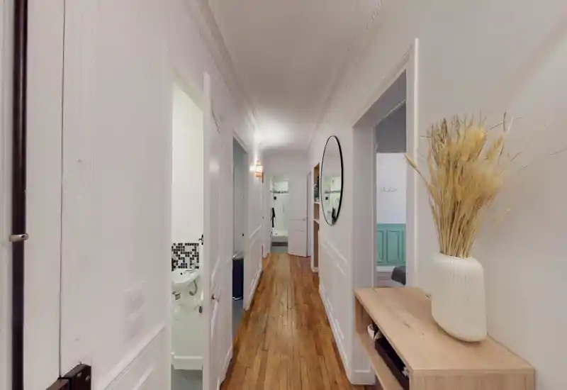 Bright, narrow entrance hallway with wooden floors, decorative mirror and console table with a vase—clean, well-lit passage connecting rooms.