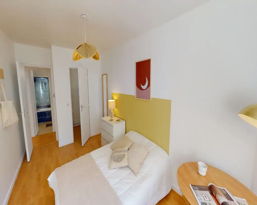 Chambre lumineuse et bien décorée avec lit double, table de chevet et éclairage chaleureux ; tons neutres et sol en bois pour une ambiance apaisante.