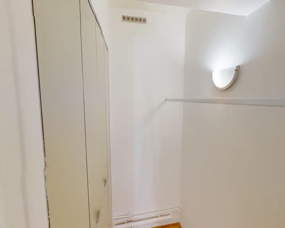 Petite zone d'entrée/placard avec des armoires intégrées, une applique murale et une tringle — espace simple, lumineux et fonctionnel.