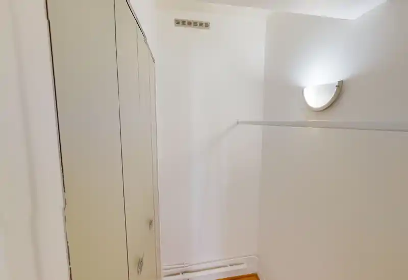 Small entrance/wardrobe area with built-in cupboards, a wall-mounted light and a hanging rail — simple, bright and functional space.