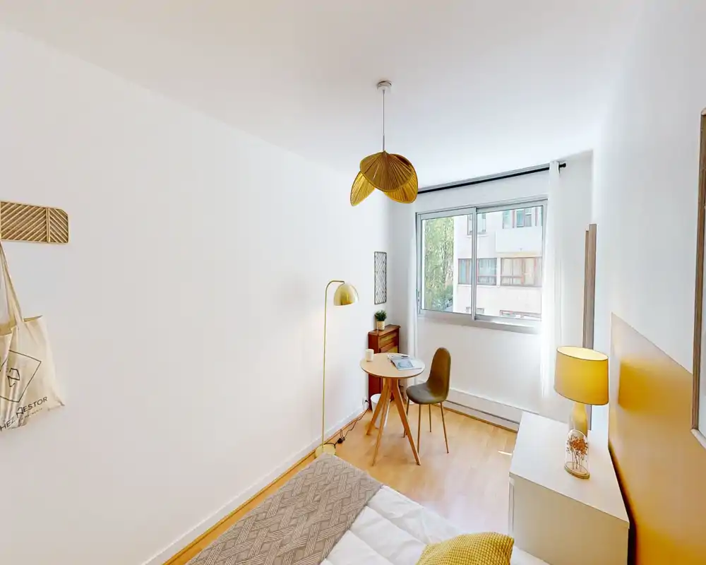 Bright, cozy single bedroom with a neatly made bed, warm lighting and a small desk by the window — ideal for a calm stay or a work corner.