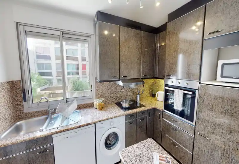 Bright, compact kitchen with granite countertops, integrated oven, sink under a large window, and built-in appliances ideal for city apartments.