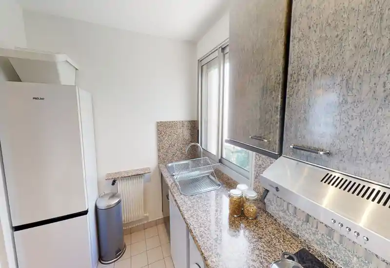 Compact, well-lit galley kitchen with granite countertops, stainless range hood, fridge and a sink under the window — neat and functional layout ideal for city apartments.