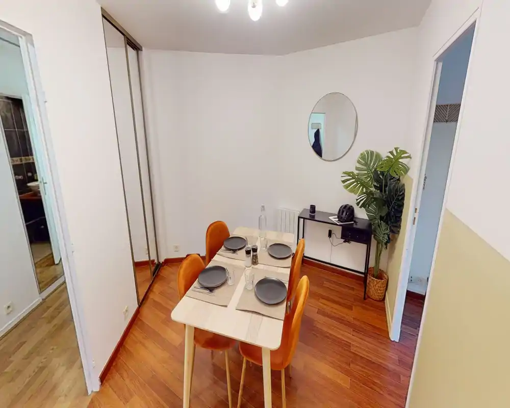 Luminoso sala da pranzo arredata con un tavolo in legno apparecchiato per quattro e sedie imbottite dai toni caldi, ideale per pasti e piccoli incontri.