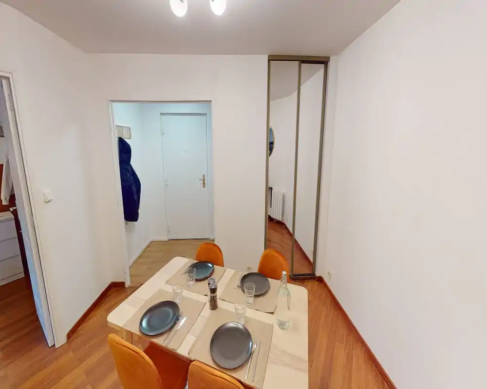 Zona pranzo ordinata con tavolo per quattro apparecchiato su pavimento in legno e sedie arancioni; ambiente semplice e ben illuminato ideale per i pasti.