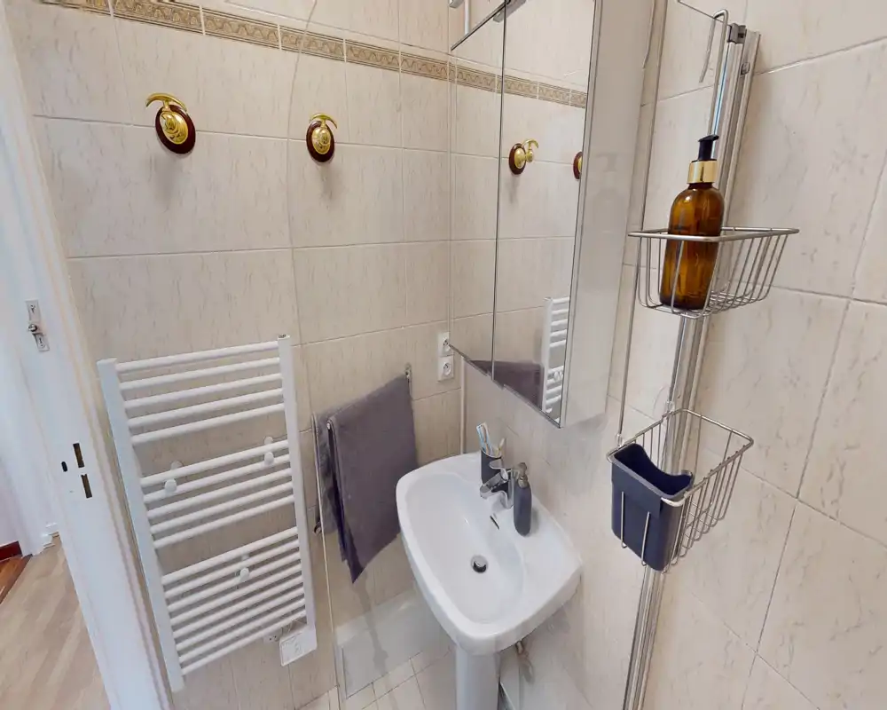 Bagno compatto e ben illuminato con lavabo a colonna, specchio con armadietto, scaldasalviette e portaricambi a parete — piastrelle pulite e arredi pratici, ideale per un soggiorno breve.