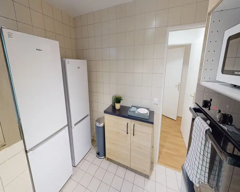 Cucina compatta e ben illuminata con due frigoriferi verticali, microonde e un piccolo mobile in legno — disposizione pratica, adatta a soggiorni brevi.