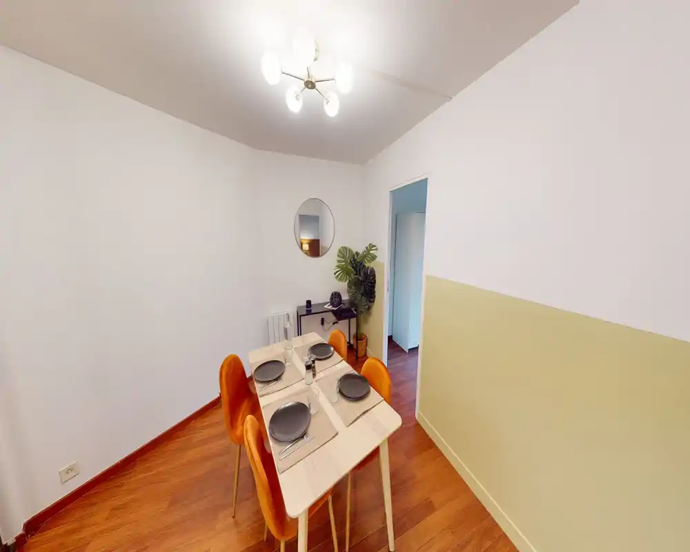 Accogliente zona pranzo ben arredata con un tavolo per quattro, sedie arancioni calde e decorazioni curate come uno specchio da parete e una pianta.