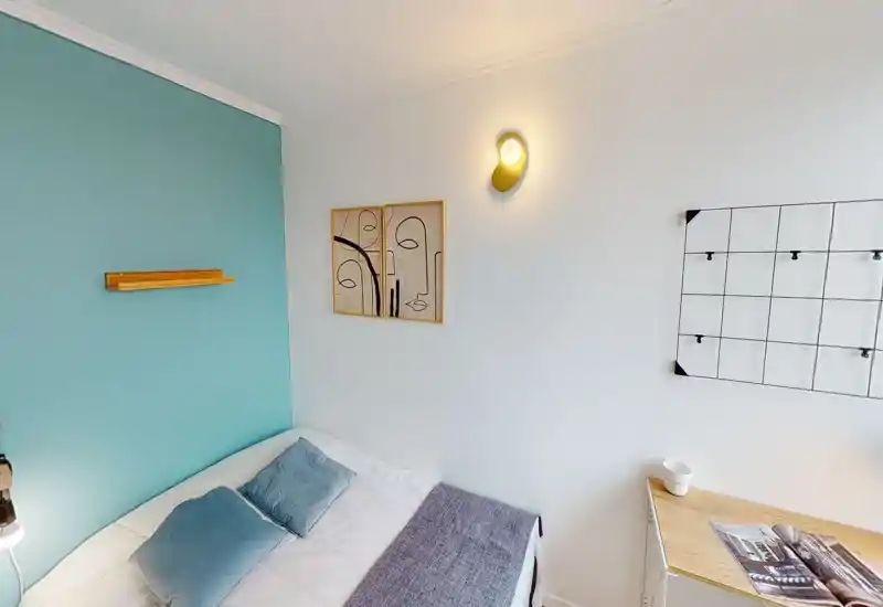 Coin chambre lumineux et chaleureux avec lit bien fait, mur d'accent turquoise, coussins décoratifs et tableau — idéal pour un séjour confortable.