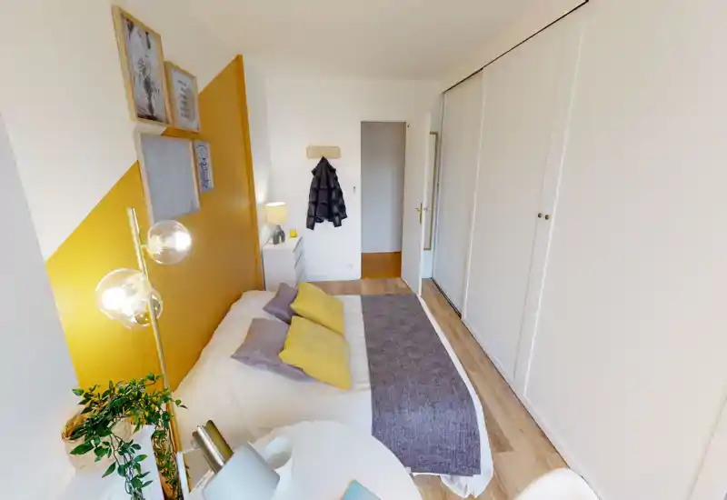 Chambre lumineuse et bien mise en scène avec lit double habillé de coussins assortis et plaid; grande armoire intégrée et table de chevet offrant des rangements pratiques.