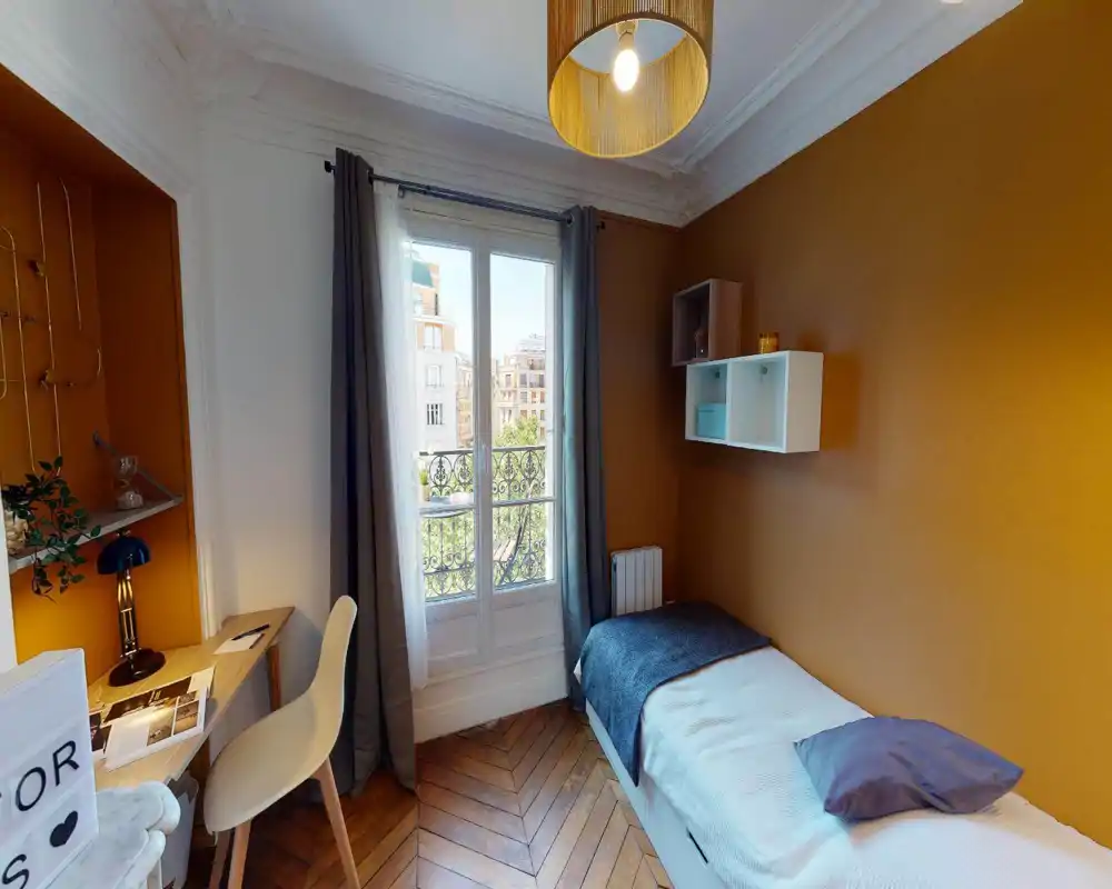 Camera singola luminosa e accogliente con letto comodo, pareti color ocra, pavimento in parquet e scrivania vicino alla finestra—ideale per studenti o viaggiatori solitari.