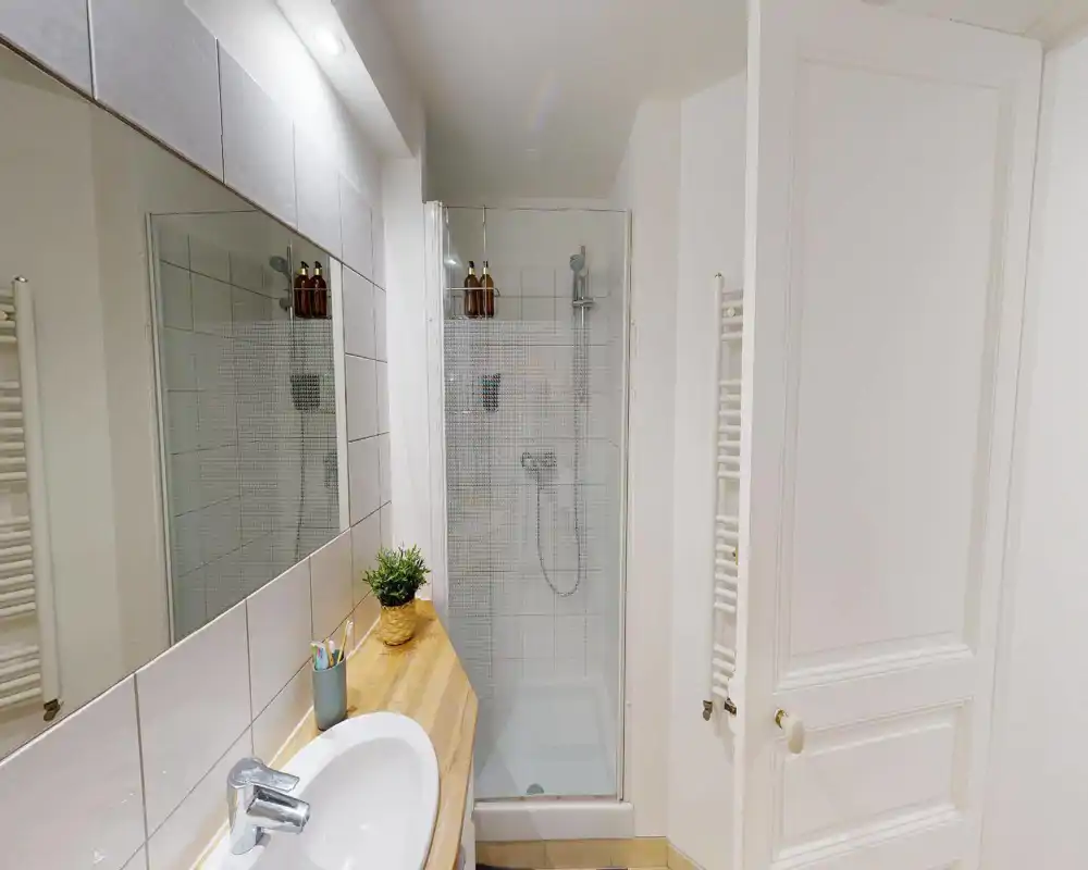 Bagno pulito e compatto con box doccia piastrellato, piano in legno con lavabo, grande specchio e scaldasalviette; stile luminoso e neutro adatto per un annuncio.