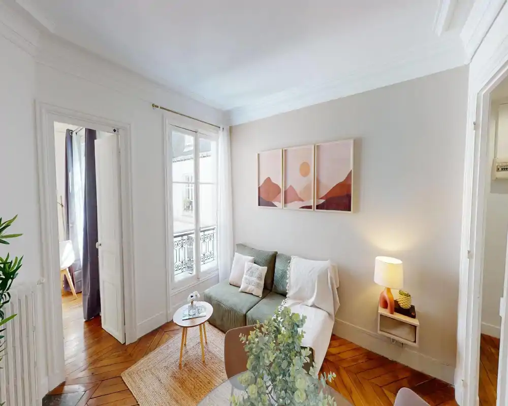 Zona giorno luminosa e di stile con un divano verde confortevole, cuscini decorativi, un piccolo tavolino e una grande finestra che fornisce luce naturale.