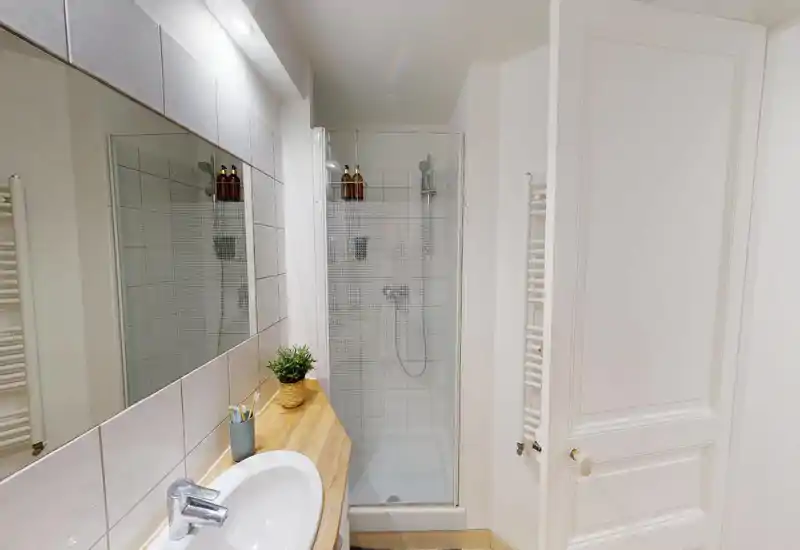 Clean, compact bathroom with a tiled shower cubicle, wooden countertop with sink, large mirror and heated towel rail; bright neutral styling ideal for a rental listing.