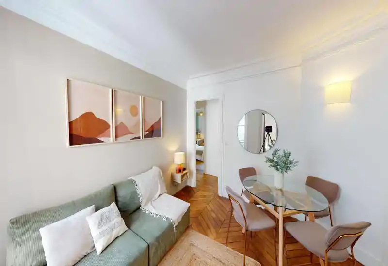 Soggiorno luminoso e di stile con divano verde confortevole, cuscini decorativi e un tavolo da pranzo in vetro vicino a uno specchio rotondo — pavimenti in legno caldi e illuminazione soffusa creano un'atmosfera accogliente.
