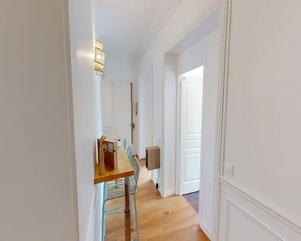 Bright, narrow entry corridor with wooden floor, wall moulding and a slim breakfast ledge with bar stools by the wall — a practical entrance/hallway area.