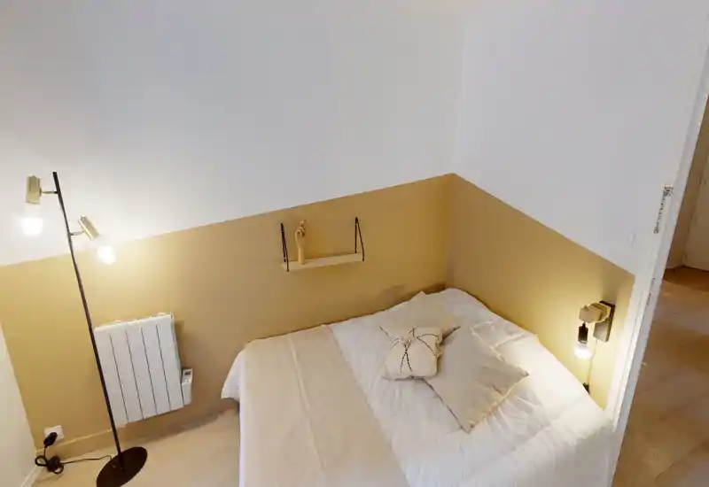 Camera da letto compatta e stilosa con letto matrimoniale in biancheria neutra, parete d'accento calda e illuminazione stratificata per un'atmosfera accogliente.