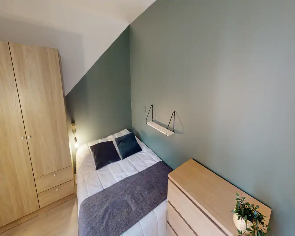 Chambre compacte et soignée avec lit double, textiles confortables et éclairage d'appoint chaleureux ; armoire et commode en bois clair pour le rangement.