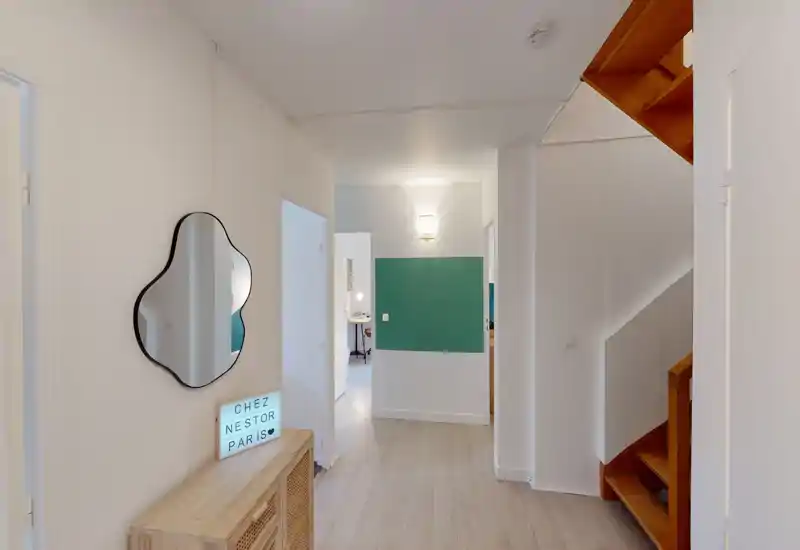 Bright, modern entrance hallway with light wood flooring, decorative mirror and a small console table; clean walls and a staircase leading up.