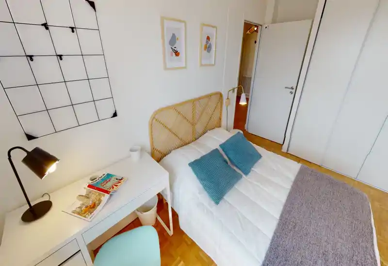 Chambre lumineuse et bien décorée avec une tête de lit en rotin, deux coussins bleu-vert et un bureau soigné au chevet — parfaite pour se reposer et travailler légèrement.