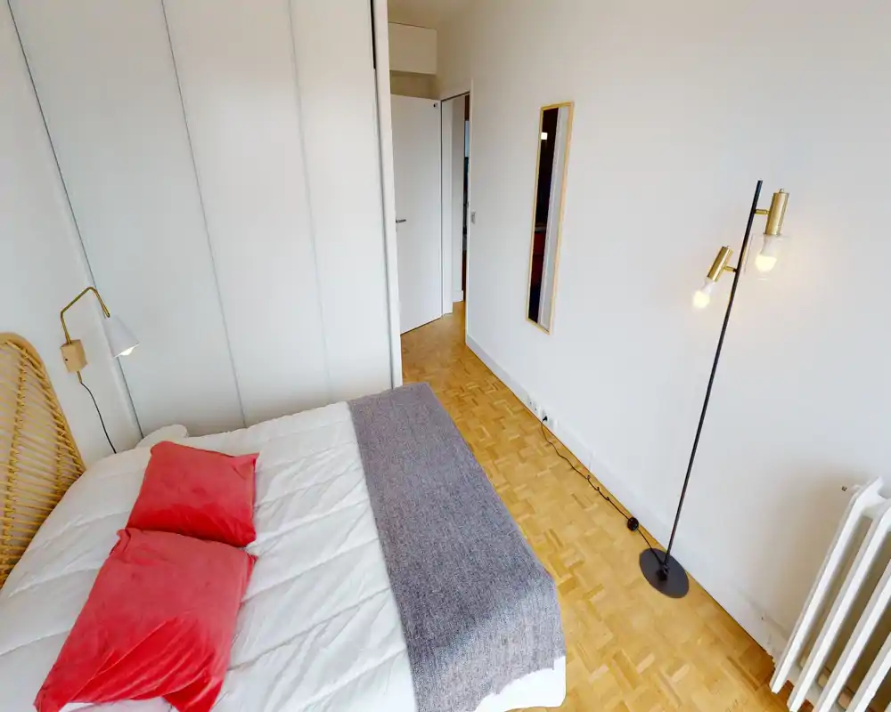 Chambre lumineuse et stylée avec un grand lit en linge blanc, coussins colorés et tête de lit en osier; sol en parquet et éclairage minimaliste pour une ambiance chaleureuse et moderne.