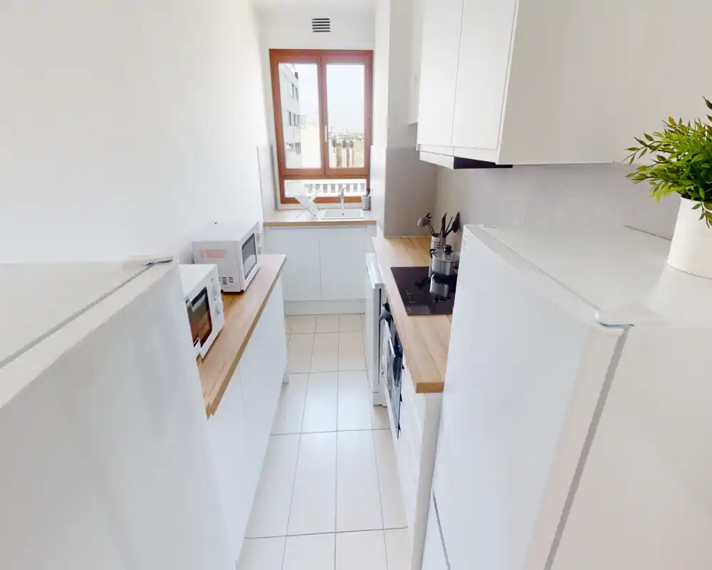 Cuisine en enfilade lumineuse et moderne avec meubles blancs, plans de travail en bois, plaque de cuisson intégrée et fenêtre apportant une belle lumière naturelle.