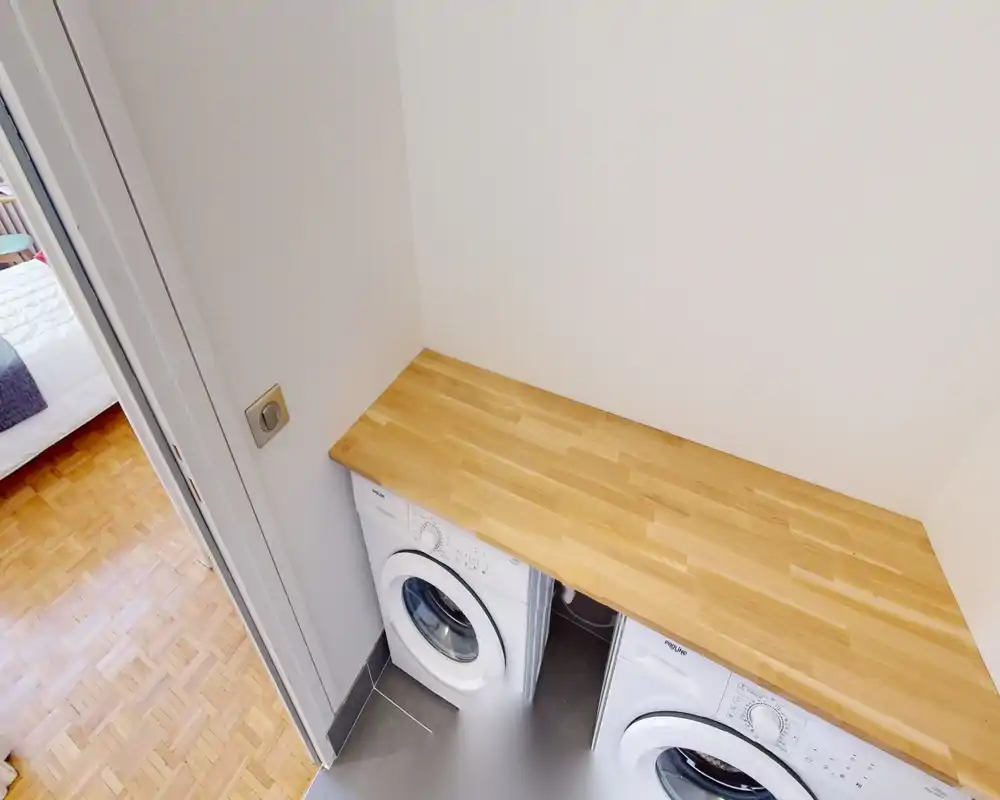 Coin buanderie compact avec deux machines à laver à hublot et un plan de travail en bois — pratique pour un appartement.