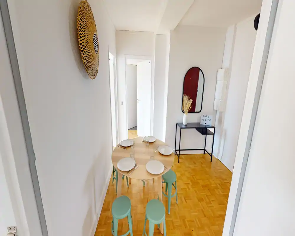 Coin repas moderne et lumineux avec une table ronde en bois dressée pour quatre et des tabourets vert menthe, accompagné d'une console et d'un miroir décoratif — un espace compact et accueillant.