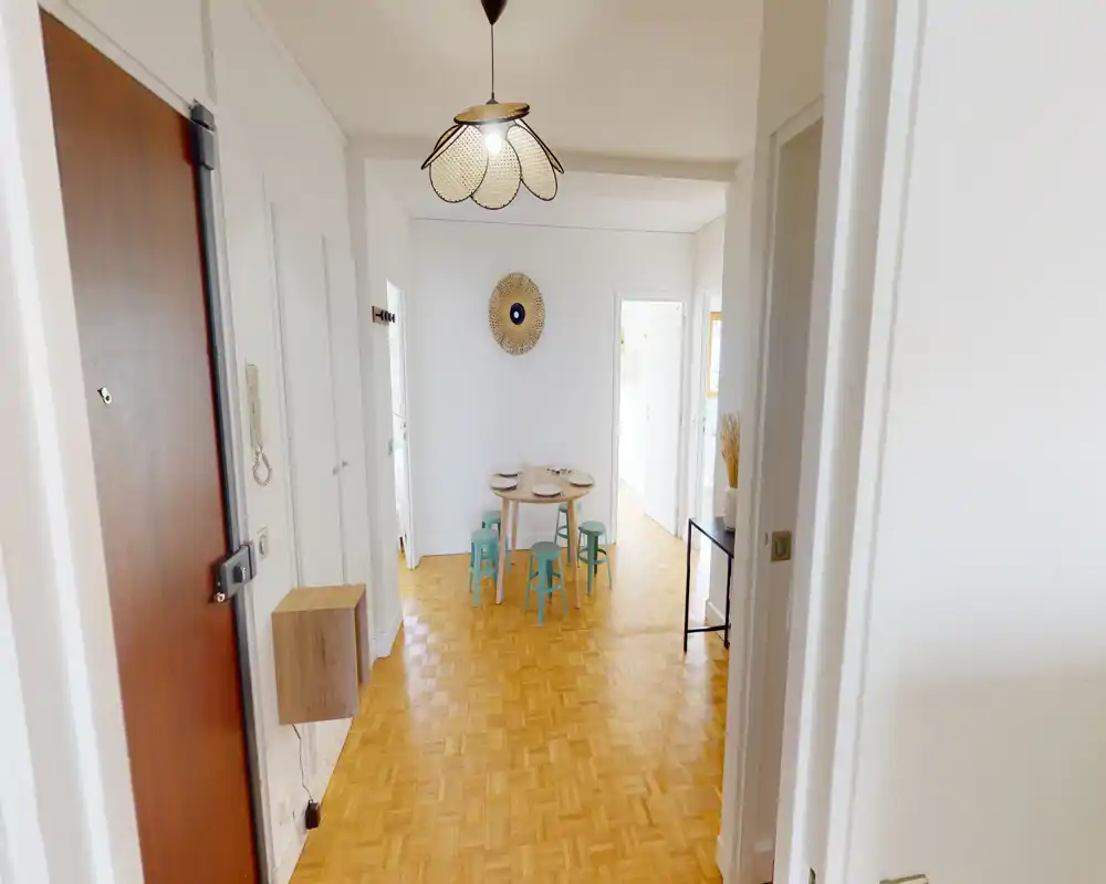 Espace repas lumineux et simple avec une petite table ronde et quatre tabourets colorés, décoration murale et parquet — idéal pour repas informels.