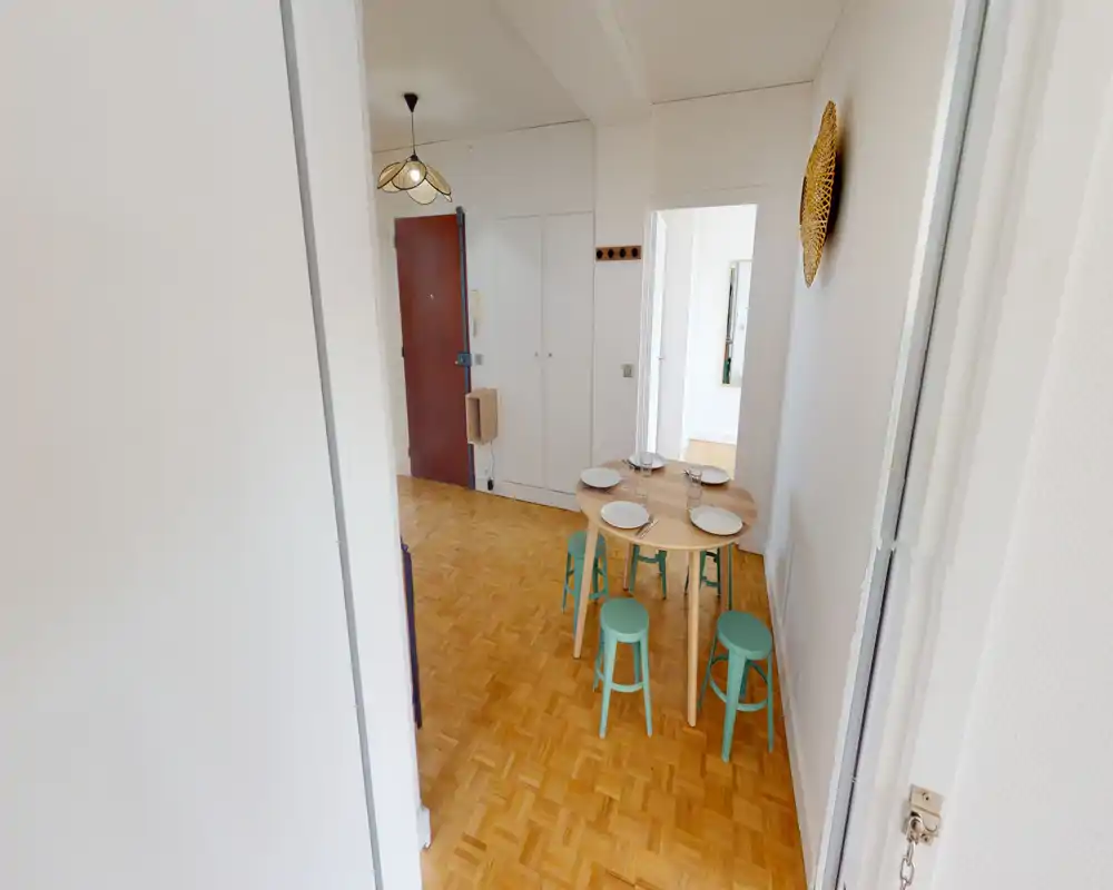 Entrée lumineuse avec parquet, table ronde dressée pour quatre et porte d'entrée visible à l'arrière — propre, simple et accueillante.