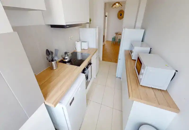 Cuisine en enfilade lumineuse avec plans de travail en bois, plaque à induction, appareils compacts et rangements soignés — parfaite pour une cuisine urbaine efficace.