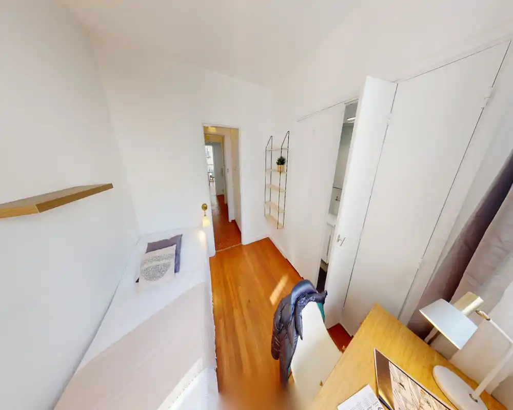 Petite chambre lumineuse avec un lit simple, parquet et un bureau compact près de la fenêtre. Décor épuré et minimal, tissus doux et belle lumière naturelle.
