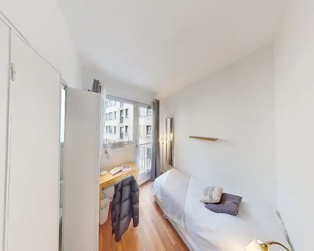 Chambre simple propre et lumineuse avec un lit confortable, un bureau en bois près de la fenêtre et un sol en parquet chaleureux — parfaite pour un étudiant ou une personne seule.
