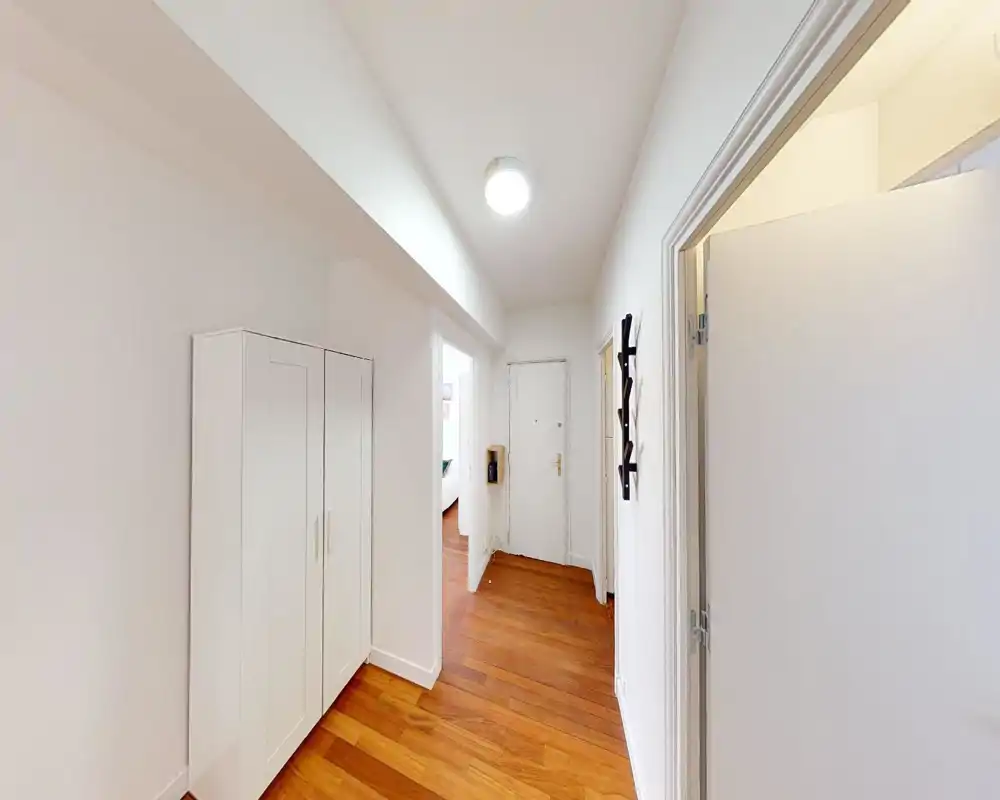 Entrée lumineuse bien éclairée avec sol en bois, une armoire blanche et un porte-manteau près de la porte — première impression accueillante.