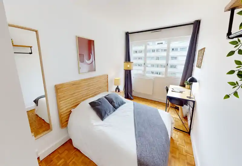 Chambre lumineuse et bien décorée avec lit double, tête de lit en bois, lampes de chevet et un petit bureau près de la fenêtre — idéale pour une ou deux personnes.