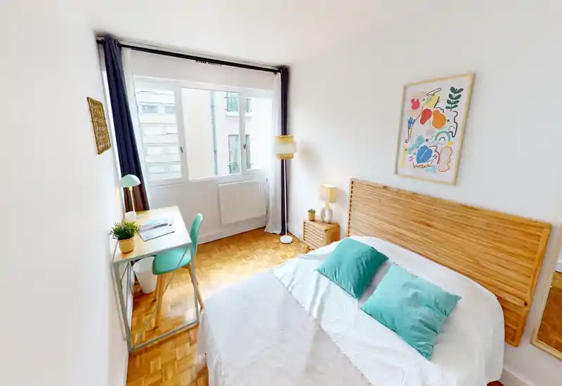 Bright, cozy bedroom with a wooden headboard, green accent pillows and a small desk by the window — ideal for restful stays and remote work.