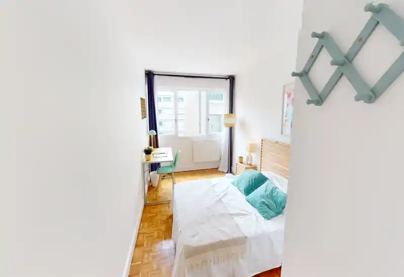Bright, well-staged bedroom with a comfortable double bed, decorative cushions and a small desk by the window offering natural light.
