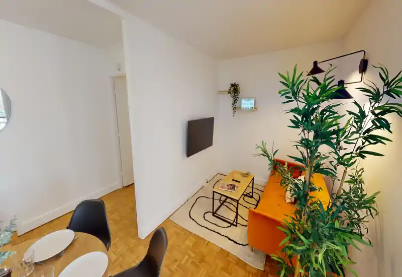 Espace de vie lumineux et tendance avec un canapé orange, TV murale, tapis décoratif et plantes d'intérieur — un coin chaleureux pour se détendre ou recevoir.