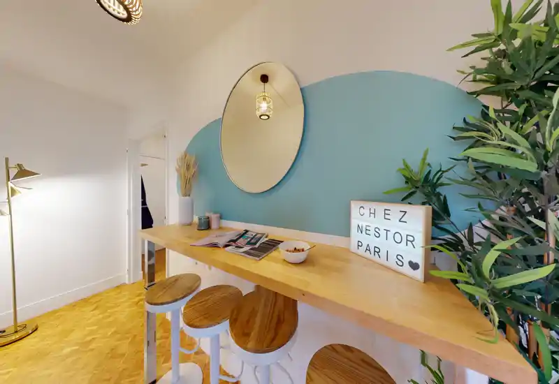Bright, styled kitchenette with a wooden breakfast bar, three stools, decorative mirror and plants — ideal for casual meals and coffee.