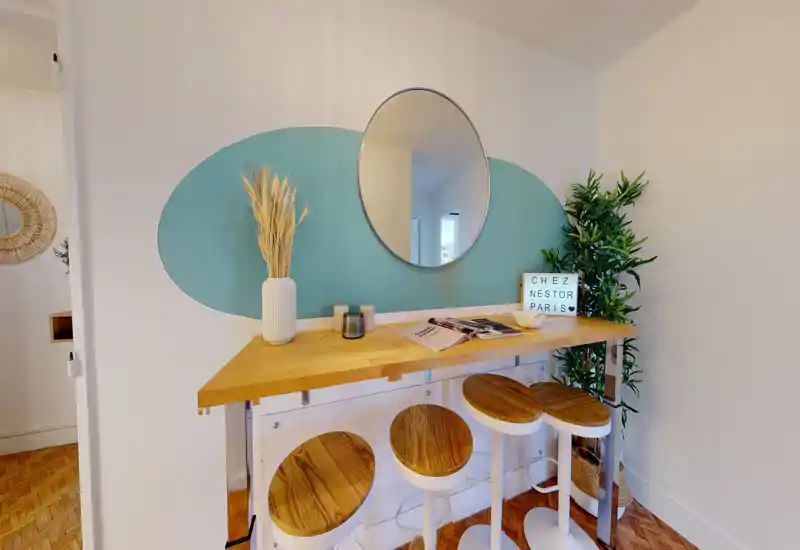 Stylish breakfast bar with three wooden stools, a light wood counter and decorative mirror — a cozy, well-lit corner ideal for quick meals or coffee.