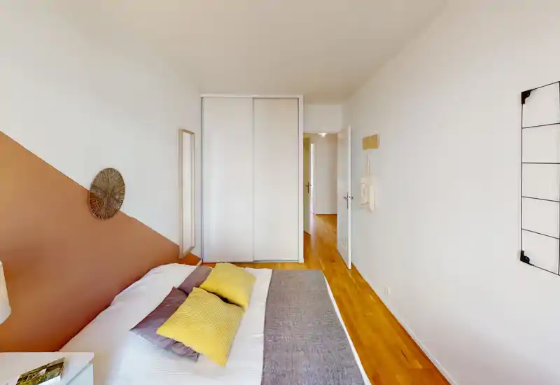 Chambre claire et bien décorée avec un lit double habillé de coussins, sol en bois chaleureux et placard intégré à portes coulissantes.