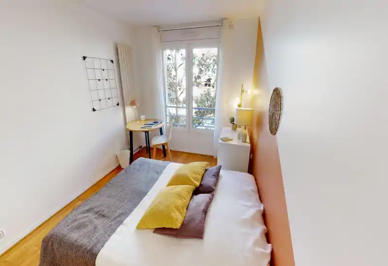 Chambre double lumineuse et bien mise en scène avec un lit confortable, un mur d'accent chaleureux et un petit bureau près de la fenêtre — parfaite pour se reposer ou travailler.
